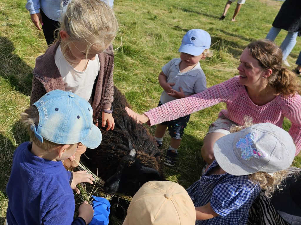 Bilden visar Magdalena tillsammans med en grupp barn som klappar ett lamm